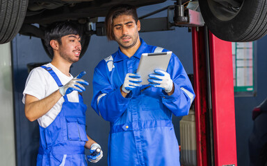 Two handsome male mechanics wearing uniform, using tablet, checking or inspecting for fix, repair car or automobile components, working in car maintenance service center or shop. Industry Concept.
