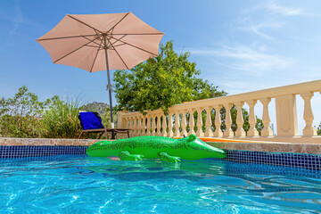 Pool mit Sonnenschirm und Krokodil-Luftmatratze im Wasser