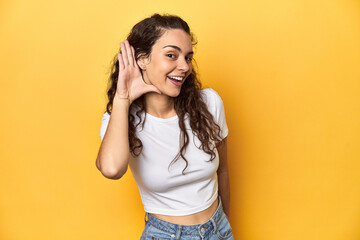 Young Caucasian woman, yellow studio background, trying to listening a gossip.