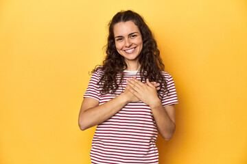 Young Caucasian woman, yellow studio background, has friendly expression, pressing palm to chest....