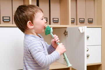 Happy toddler baby with a cleaning brush in the house. A funny child is holding a large brush in...