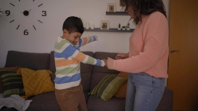Young woman and child improvise fashionable dance in living room at home. Single parent Latin family having fun together in free time. Excited and cheerful mother and son couple listening to music.