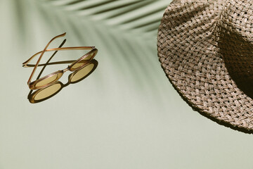 Summer flat lay with straw hat and sunglasses on green background with palm leaf shadow, sun and...