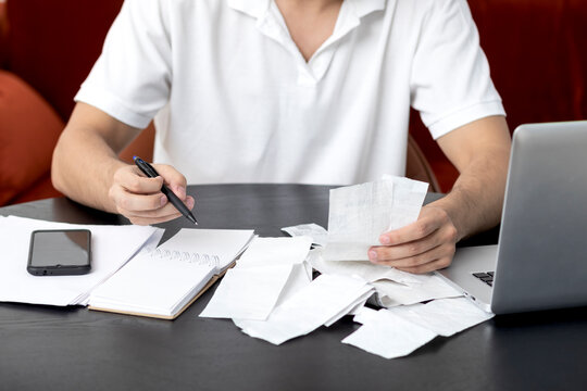 Close up of unhappy man sitting at the table, stressed and confused by calculate expense from invoice or bills, have no money to pay mortgage or loan. High prices and spending money concept