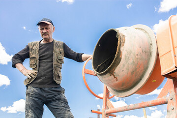 concrete mixer on the street and a man worker during the day in summer.