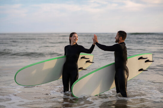 Happy Man And Woman In Wetsuits Giving High Five After Surfing Together