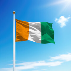 Waving flag of Ivory Coast on flagpole with sky background.