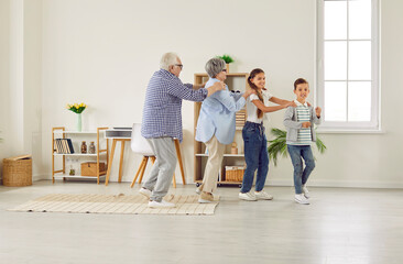Happy family spending time at home and having fun together. Funny grandparents and children play games and dance conga line. Little kids with granny and granddad walk in line like train in living room - obrazy, fototapety, plakaty