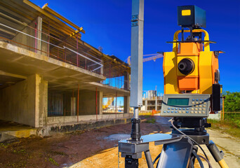 Equipment for surveyor. Construction site. Geodetic device on tripod. Gadget for work of surveyor. House under construction under blue sky. Yellow geodetic device. Equipment for builder - surveyor