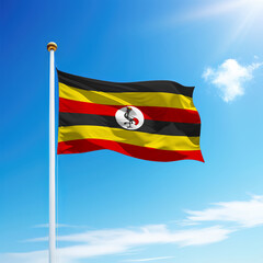Waving flag of Uganda on flagpole with sky background.