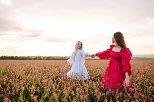 Two woman in stylish summer dresses feeling free in the field with flowers in sunshine. Nature, vacation, relax and lifestyle. Summer landscape.