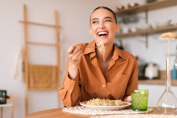 Kitchen happenings. Excited woman eating tasty homemade pasta, sitting in cozy kitchen interior,...