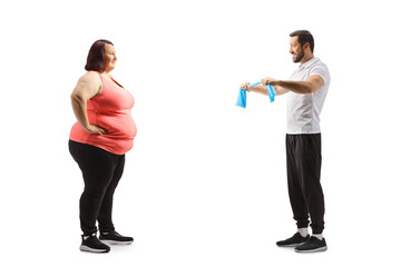 Full length profile shot of a fitness trainer showing an exercise to an overweight young woman