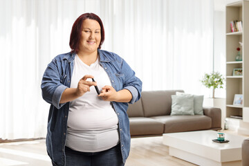 Overweight woman poking finger with an insulin pen at home and looking - obrazy, fototapety, plakaty