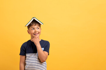 Happy school aged boy with book on head, copy space