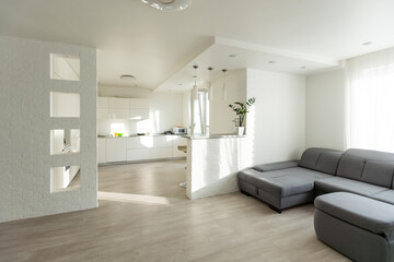 White kitchen interior with rest zone, sofa and cooking set near panoramic window with countryside. Shelf rack with decoration on hardwood floor, 3D rendering