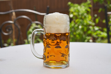 Traditional style half litre mug full of cold pilsner beer made from hop, barley and spring water, brewed in Czech republic on the table with white table colth in beer garden in hot, sunny summer day.