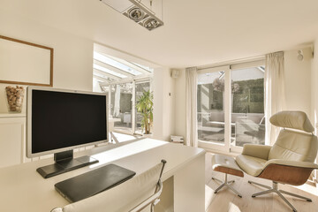 a living room with a flat screen tv on the wall and an office chair next to it in front of a large window