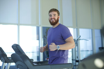 Fototapeta na wymiar Happy young fit man training in the gym, running jogging on treadmill, doing cardio exercise and smile. Healthy lifestyle, sport, fitness concept