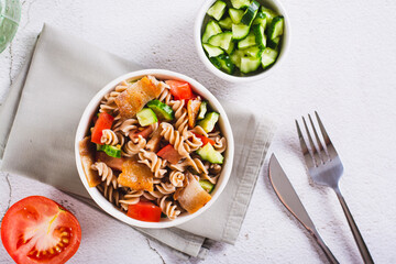 Hearty salad of pasta, cherry tomatoes, cucumbers and fried bacon in a bowl top view
