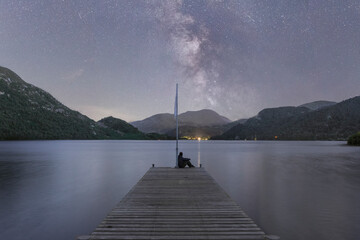 Lone person watching the Milky way on a jetty by a lake