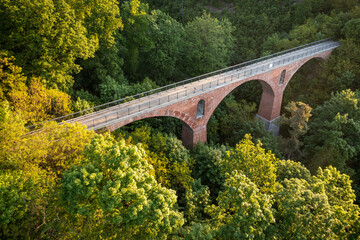 Aerial view of a red brick arch railroad bridge spanning over a lush green forest