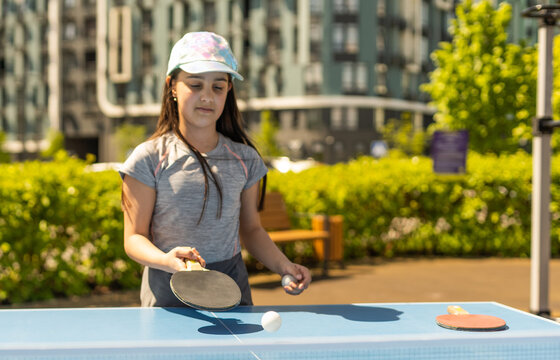Young teenager girl playing ping pong. She holds a ball and a racket in her hands. Playing table tennis outdoors in the yard