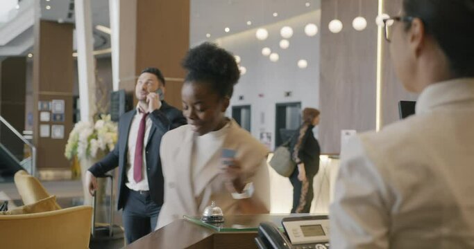 Multi-ethnic entrepreneurs are getting key cards at reception desk in modern hotel talking to administrator discussing accommodation