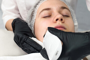 Cosmetologist making facial treatment with ultrasonic spatula to young woman. Ultrasound facial...