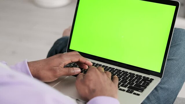Black man using laptop notebook viewing green screen press keyboard browsing chroma key, African American freelancer online typing text working remotely on computer close up from home.