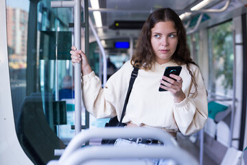Young attractive lady tram passenger using mobile phone during her travel