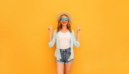 Cheerful young woman posing wearing summer straw hat and shorts on orange background