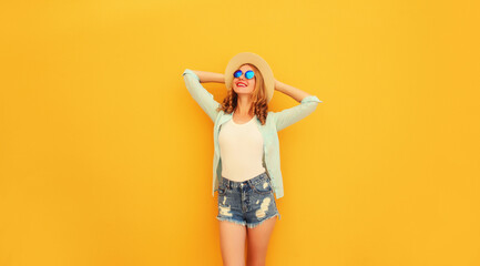 Happy caucasian relaxed young woman wearing shorts, summer straw hat on yellow background