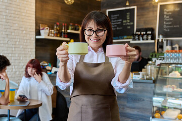 Portrait of smiling female coffee shop worker holding two cups of coffee in hands