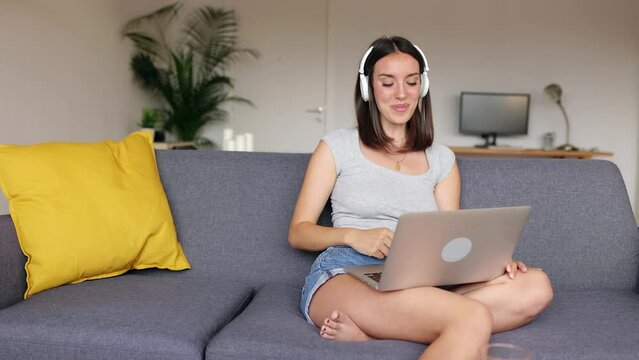 Happy young woman talking on laptop video call studying online from home. Beautiful student girl connected at online training virtual class relaxing on couch. Education and technology concept.