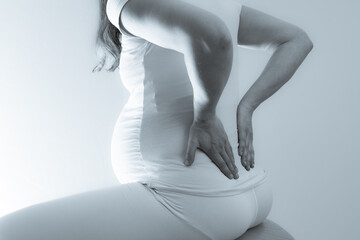 Pregnant mother with baby bump on gymnastic ball feels back pain and holds hands on her aching...