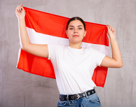 Calm girl cheerleader holding Austrian flag in her hands .Isolated on gray background