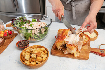 woman prepares a caesar salad in the kitchen. Pieces of fried chicken are added to the salad bowl. Knife and hands close-up.