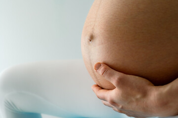 Atmospheric closeup of heavily pregnant baby belly held by hands of mother sitting on gym ball....