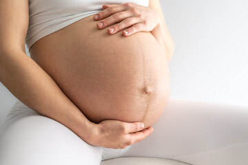 Midsection of a woman sitting on a stool and gently holding her very round pregnant baby belly....
