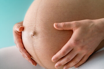 Closeup of a sitting woman gently holding her very round pregnant baby bump. Side angle view. Turquoise background. Bright shot. Black and white.