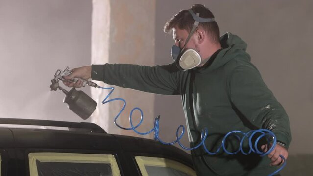 Automotive painting, Car painting, Auto painting. Man in respirator diligently spray painting car.
