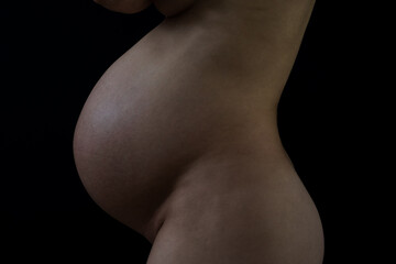 Middle part of unrecognizable standing naked mother with round pregnant baby belly. Final month of pregnancy - week 36. Side view. Black background. Black an white.