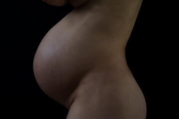 Middle part of unrecognizable standing naked mother with round pregnant baby belly. Final month of...
