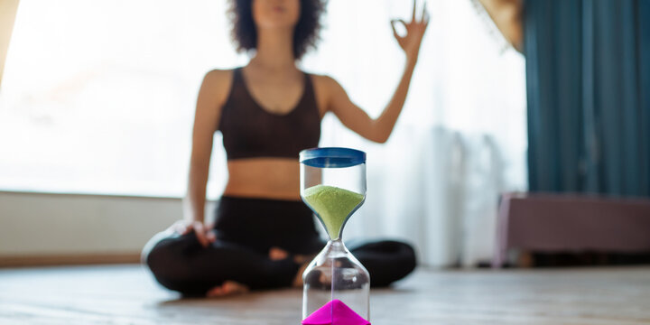 Hourglass and candle with woman and yoga class in the background. Yoga and mind. Health and body wellness concept. Skin relaxation and treatment. Healing salt lamp.