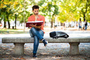 Handsome young man reading book on bench in the park