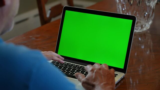 A reverse over the shoulder (OTS) shot of a man video chatting on his laptop, perhaps with his grandchildren. Green screen for custom content. Complimentary front version available.  	