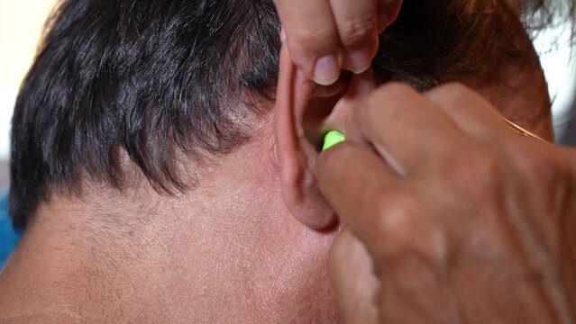 A detailed view of a man properly inserting a foam ear plug.  	