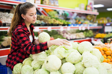 Portrait of a young female customer in a store near the counter, choosing cabbage to buy