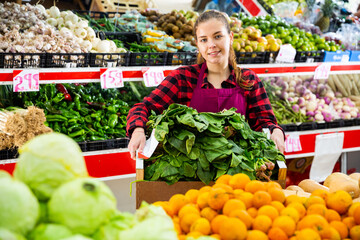 Young smiling woman salesman carrying box with fresh spinach at supermarket